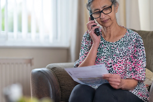 Customer sat in her living room on the phone, looking at a bill